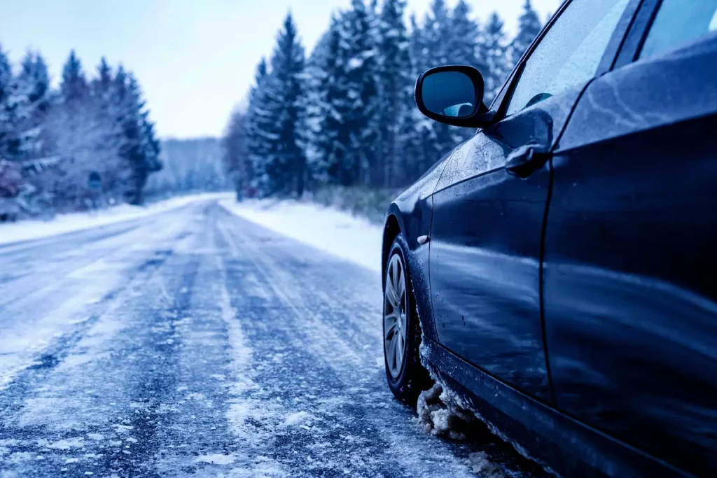 black car iced road surrounded by trees covered with snow